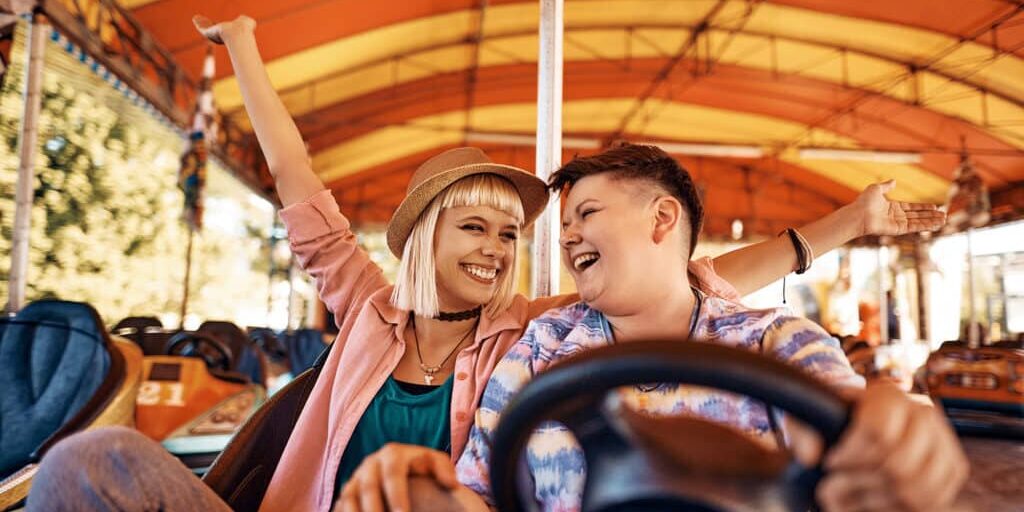 Carefree same-sex couple driving bumper car and having fun together at amusement park.