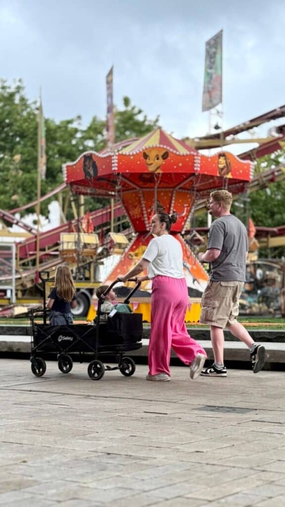 Family sitting on a bench in a theme park courtyard with children snacking and a stroller parked nearby